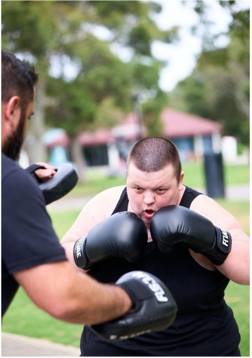 Participant boxing outdoors with a support worker holding the pads